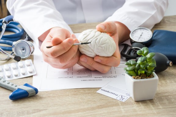 At doctors appointment, a physician shows to patient shape of brain with focus on hand with organ. Scene explaining patient causes and localization of diseases of brain, nerves and nervous system.