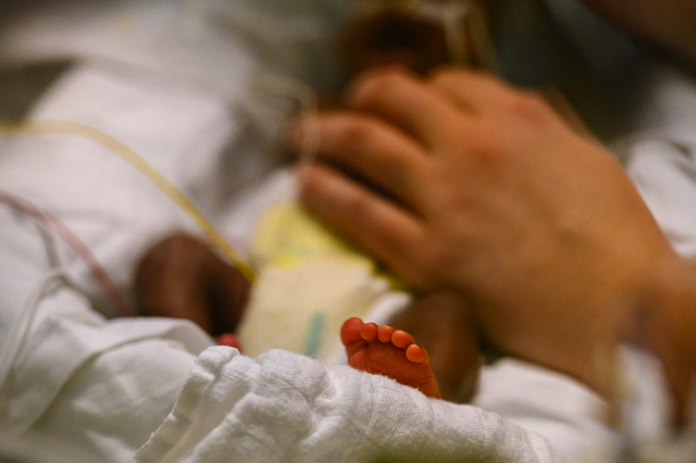 A small baby in a bed, with an adult hand tending to the baby.