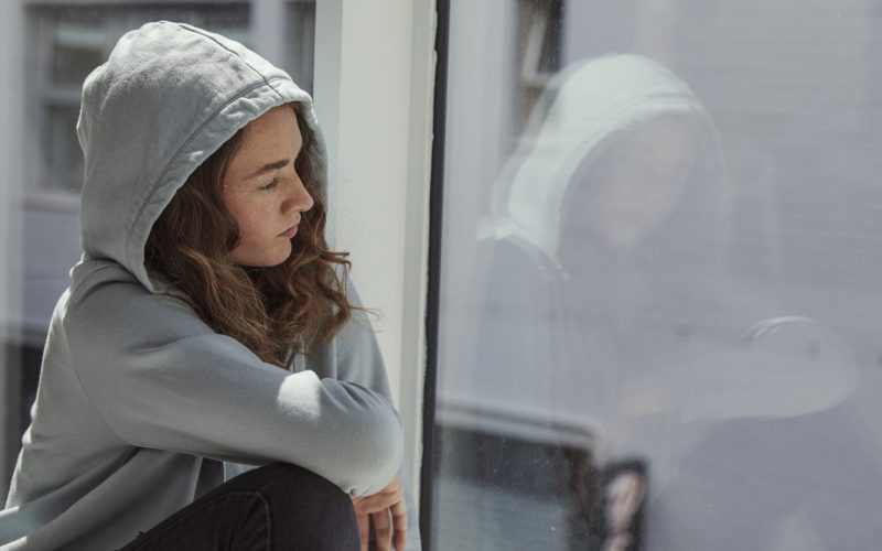Side view young woman looking away at window sitting on the floor in the school.