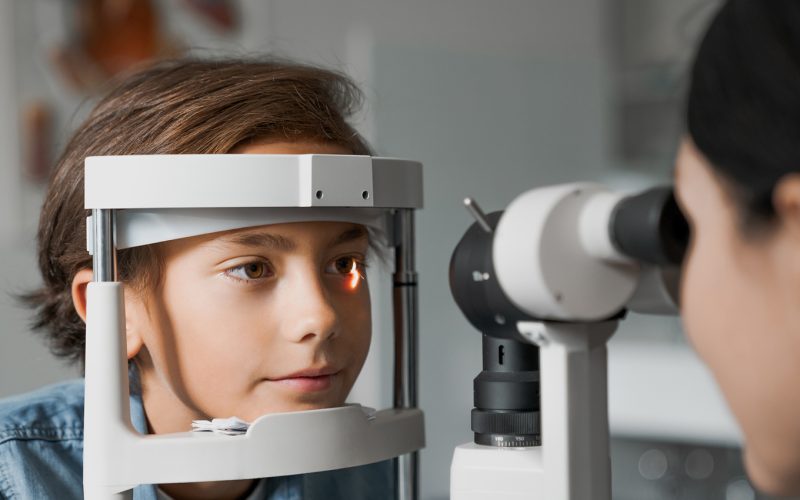 Adult female doctor ophthalmologist is checking the eye vision of cute child in modern clinic