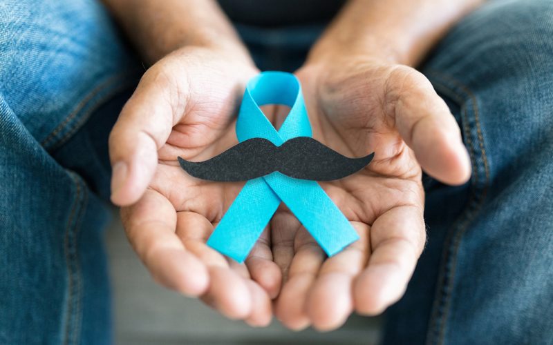 Senior man holding a blue cancer awareness ribbon with a black moustache