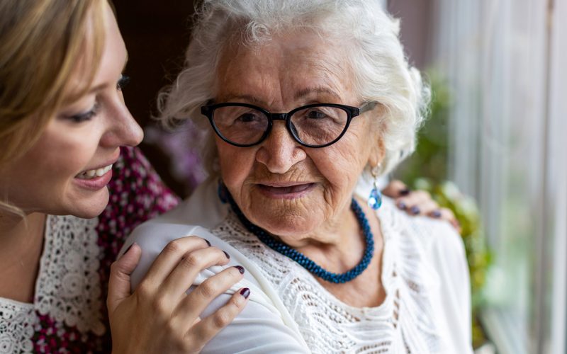 A younger woman places her hands on the shoulders of an older lady