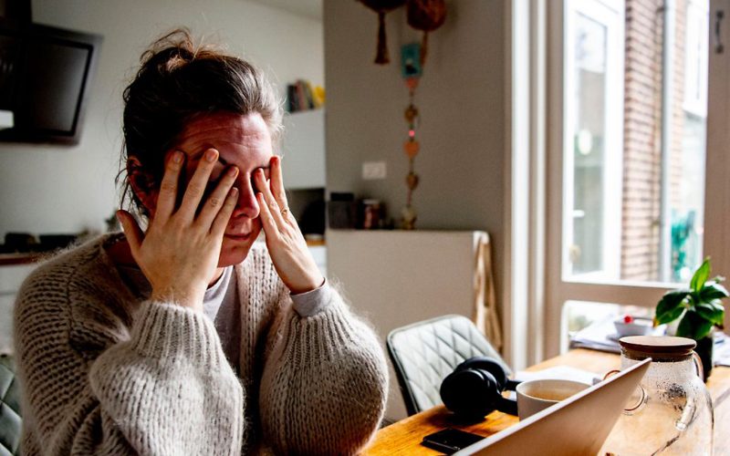 A Woman sits behind her laptop with her hands over her eyes