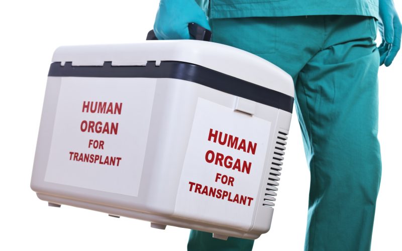 A person in scrubs carries a box with the text 